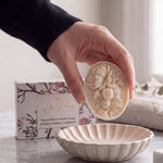 Lise Fiola Creations botanical artisanal soap with intricate floral relief design held above a matching soap dish.