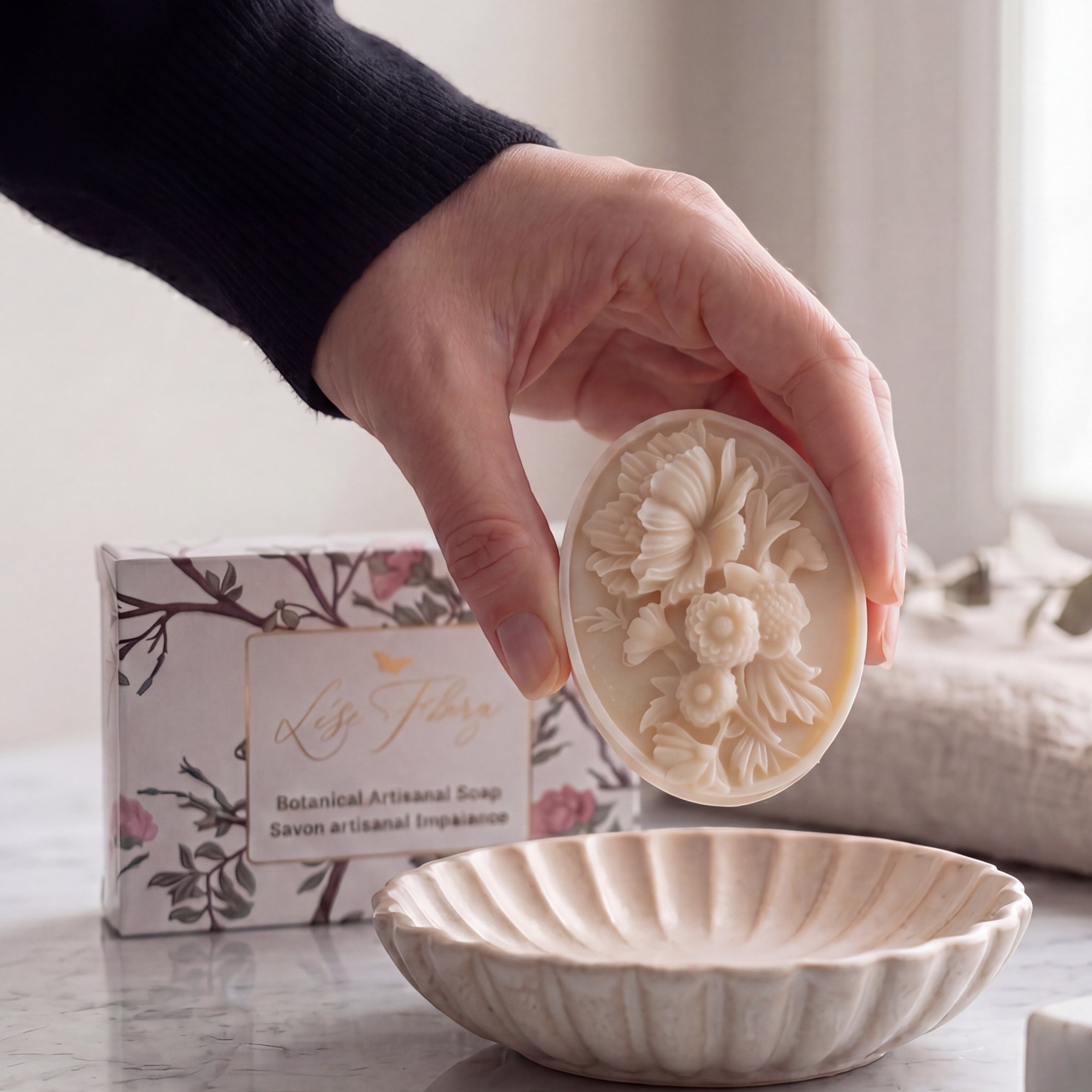 Lise Fiola Creations botanical artisanal soap with intricate floral relief design held above a matching soap dish.