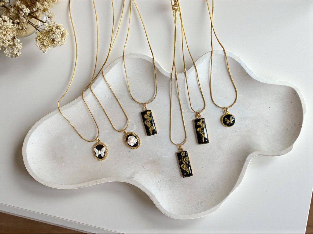 Lise Fiola Creations collection of gold-plated necklaces featuring polymer clay roses and floral designs on black